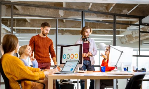 Group of young coworkers dressed casually working together on the computers with some charts sitting in the modern office interior